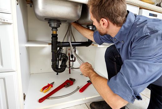 Plumber repairing pipes under a kitchen sink.