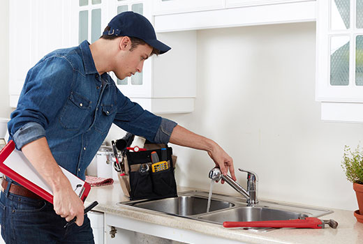 Plumber testing water flow from a repaired stainless steel kitchen sink faucet.