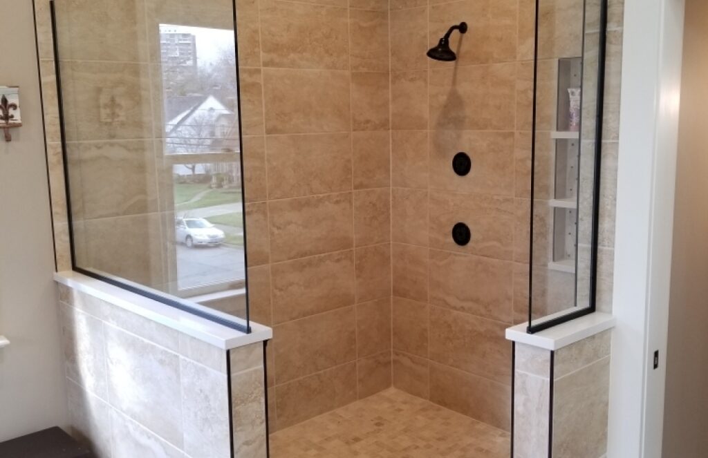 Newly installed corner shower with light tan tiles, black fixtures, walk-in style.